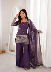 Woman in a purple traditional outfit with gold details standing in a bright room.