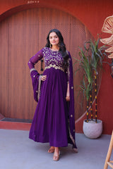 Woman in a purple traditional outfit standing against a red wall with decorative elements.