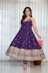 Woman wearing a purple anarkali suit with gold embroidery against a white curtain background