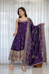 Woman wearing a purple traditional outfit with a matching dupatta against a white curtain background