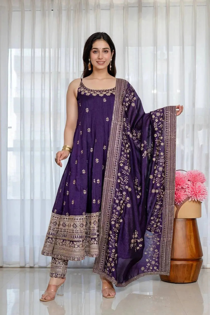 Woman wearing a purple traditional outfit with a matching dupatta against a white curtain background