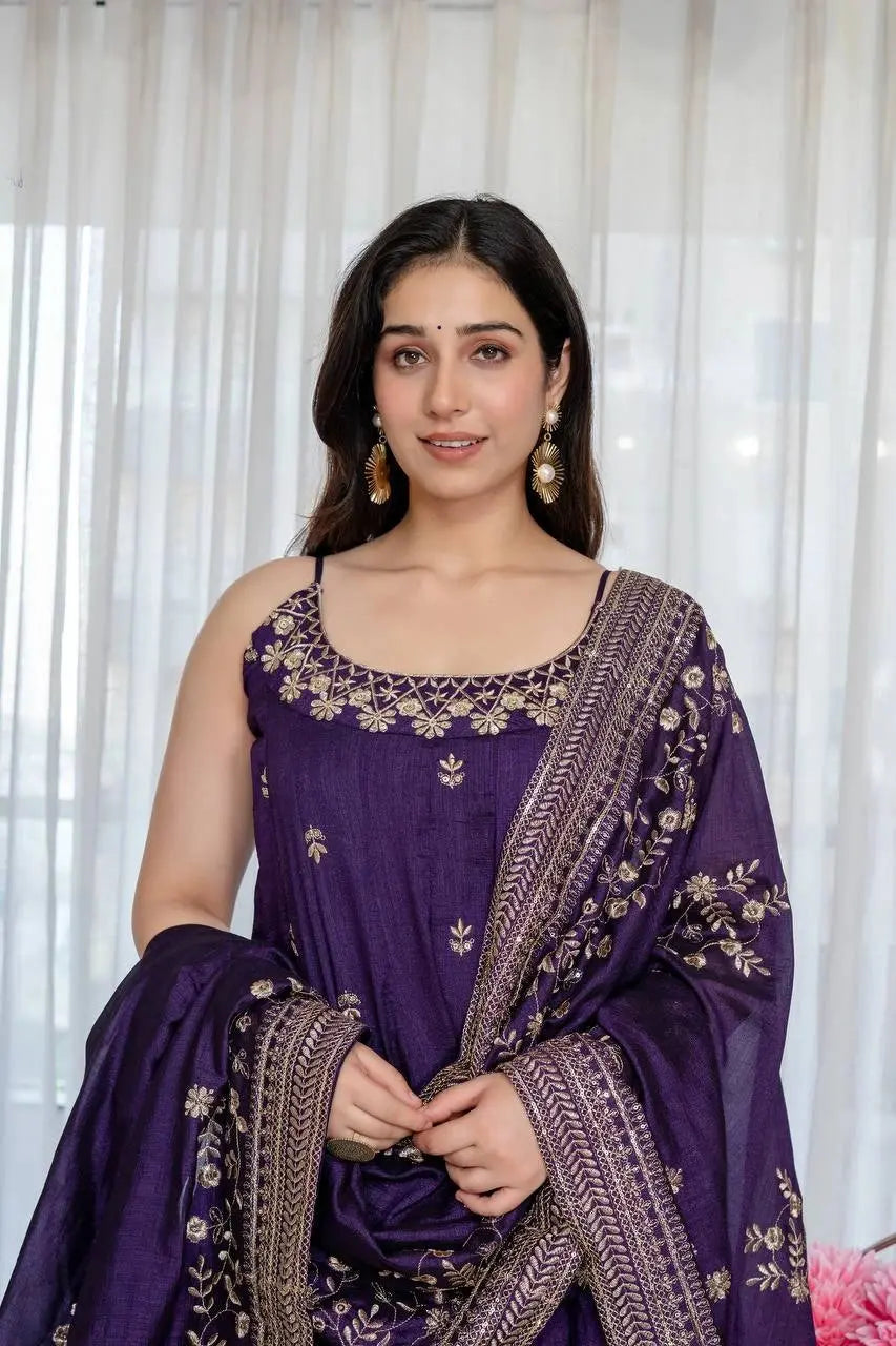 Woman wearing a traditional purple outfit with gold embroidery against a white curtain background