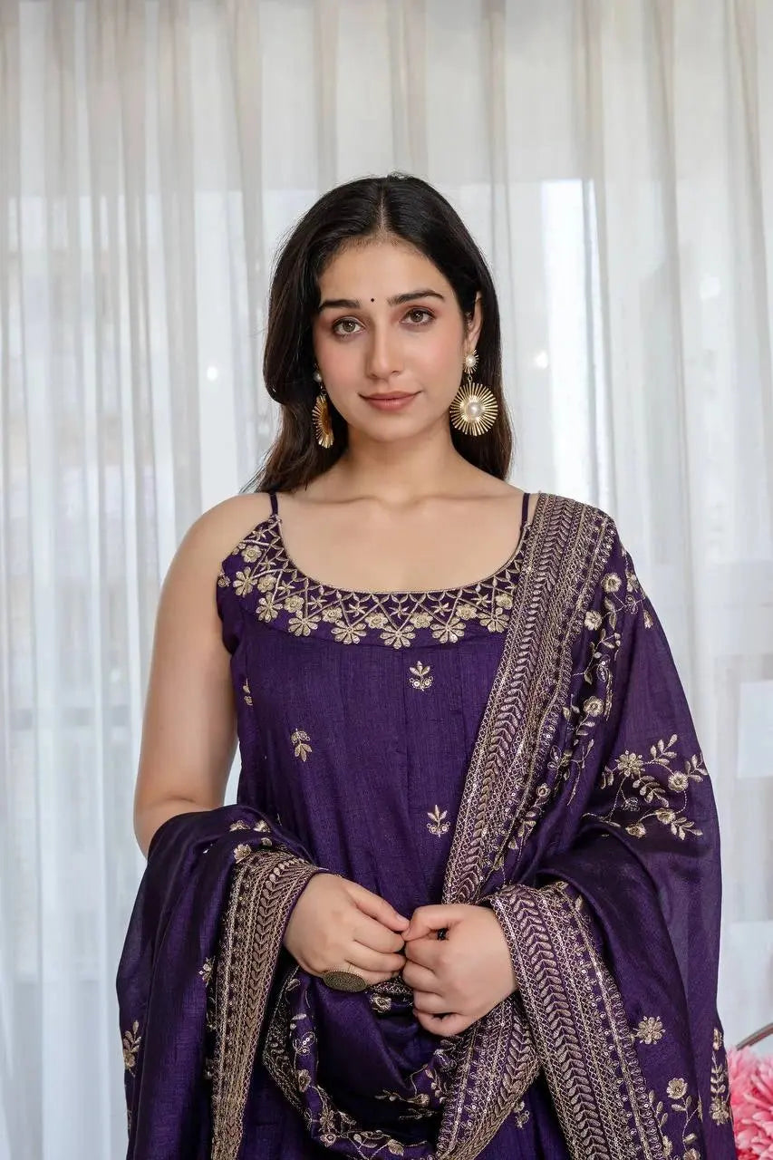 Woman wearing a purple traditional outfit with gold embroidery against a white curtain background