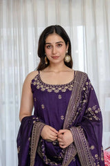 Woman wearing a purple traditional outfit with gold embroidery against a white curtain background
