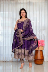 Woman in a traditional purple outfit with intricate patterns standing in a well-lit room.
