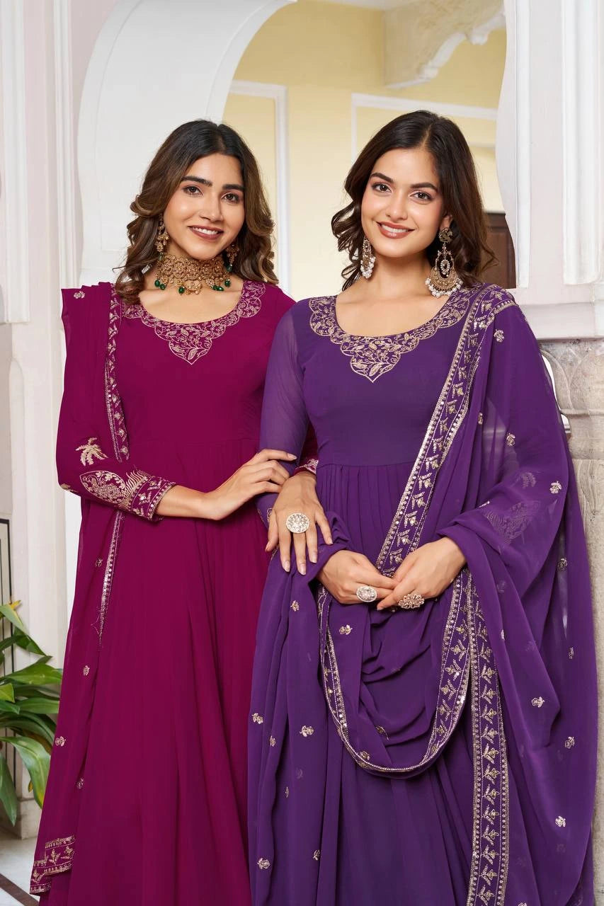 A medium shot of two women posing together. One wears a magenta Anarkali and the other a deep purple one. Both suits feature intricate gold zari embroidery around the scoop neckline and sequin-bordered dupattas.