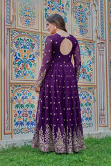 Woman in a purple dress with cut-out back standing in front of a colorful patterned wall.