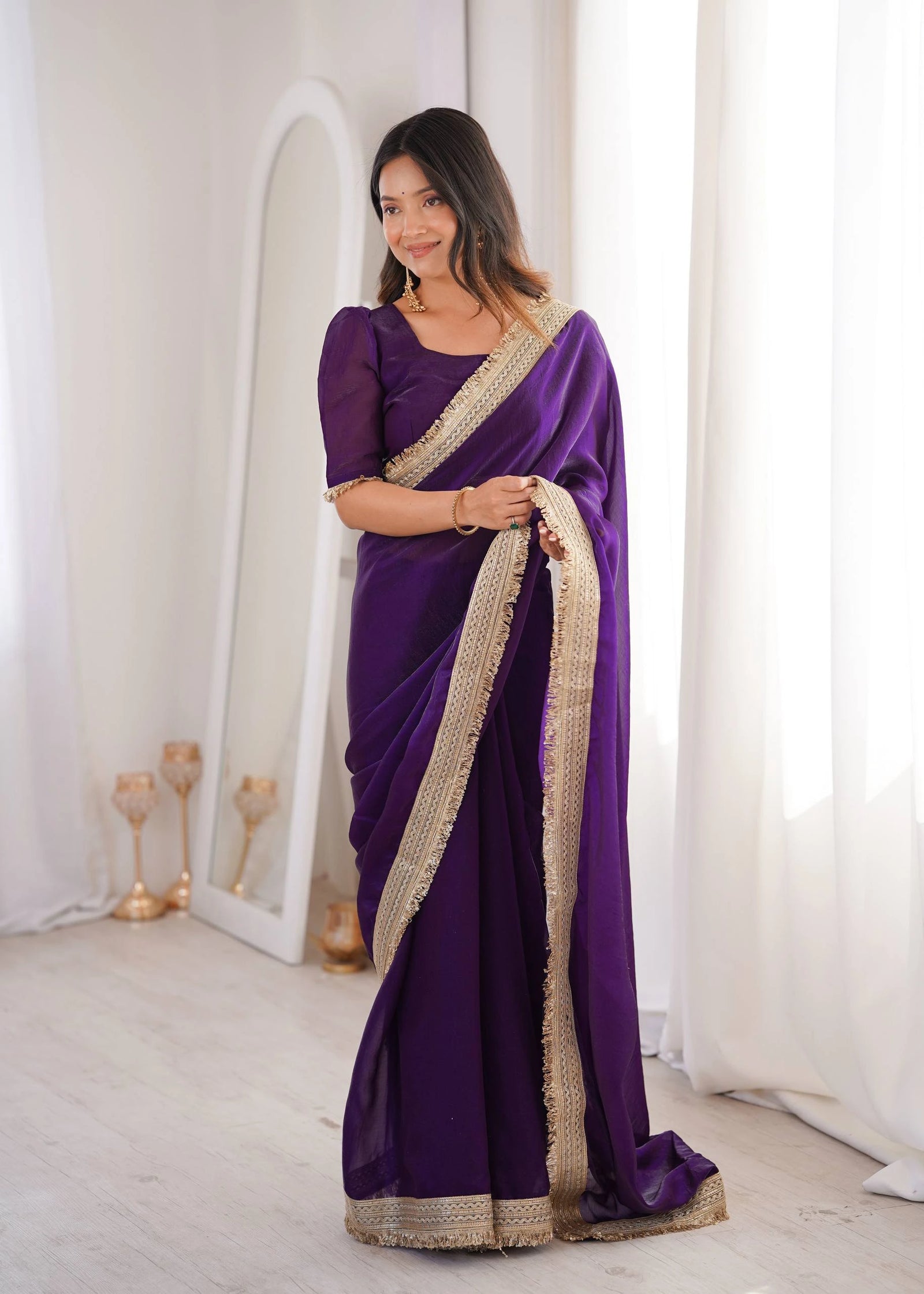 Woman wearing a purple saree with gold border indoors.