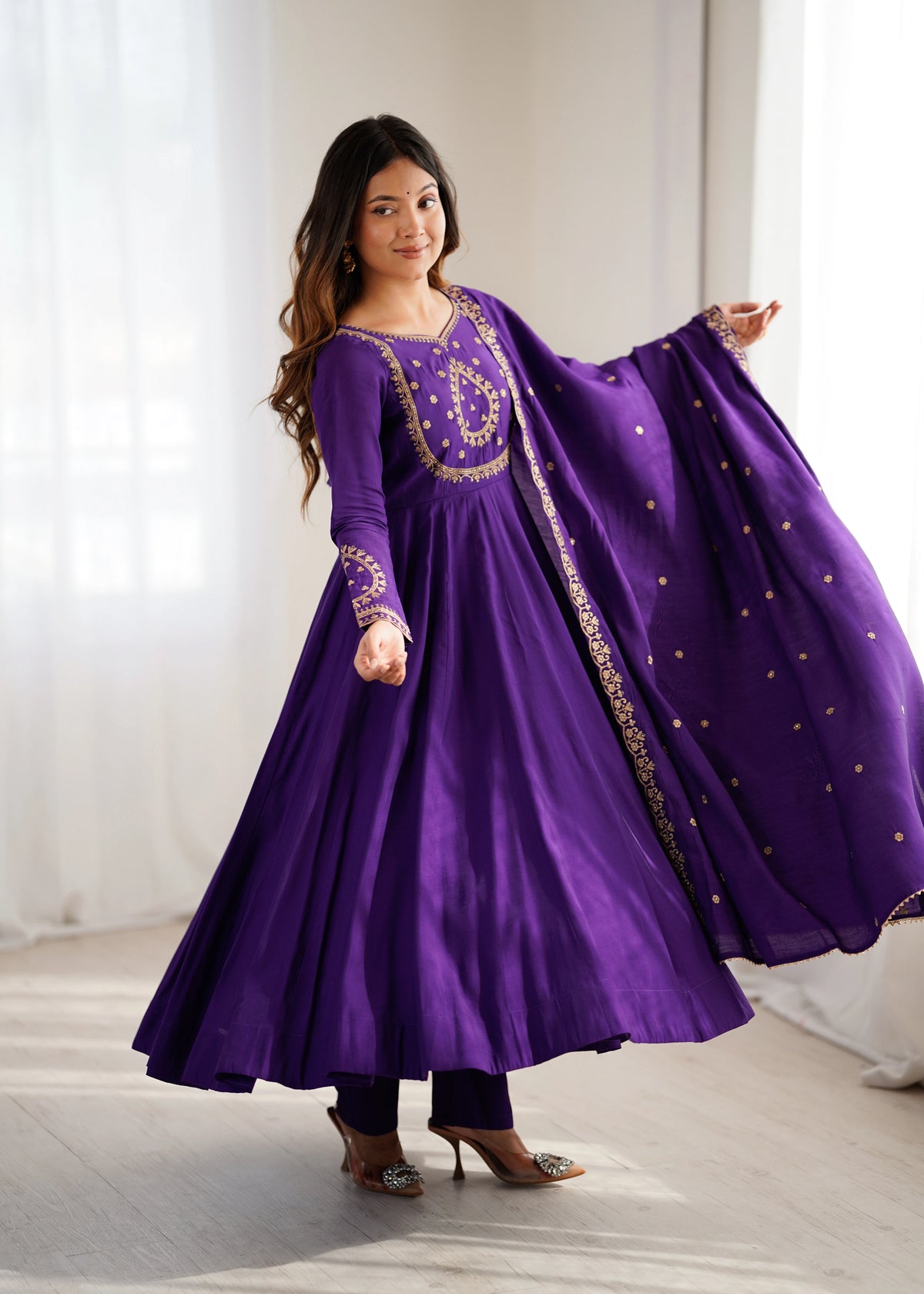 Woman wearing a purple traditional outfit with gold embroidery in a bright room.