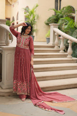 Woman in a traditional pink embroidered outfit standing on steps with decorative elements.