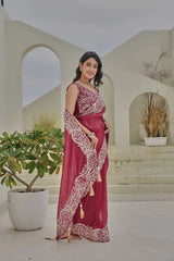 Woman in a red saree with white patterns standing in a decorative outdoor setting.