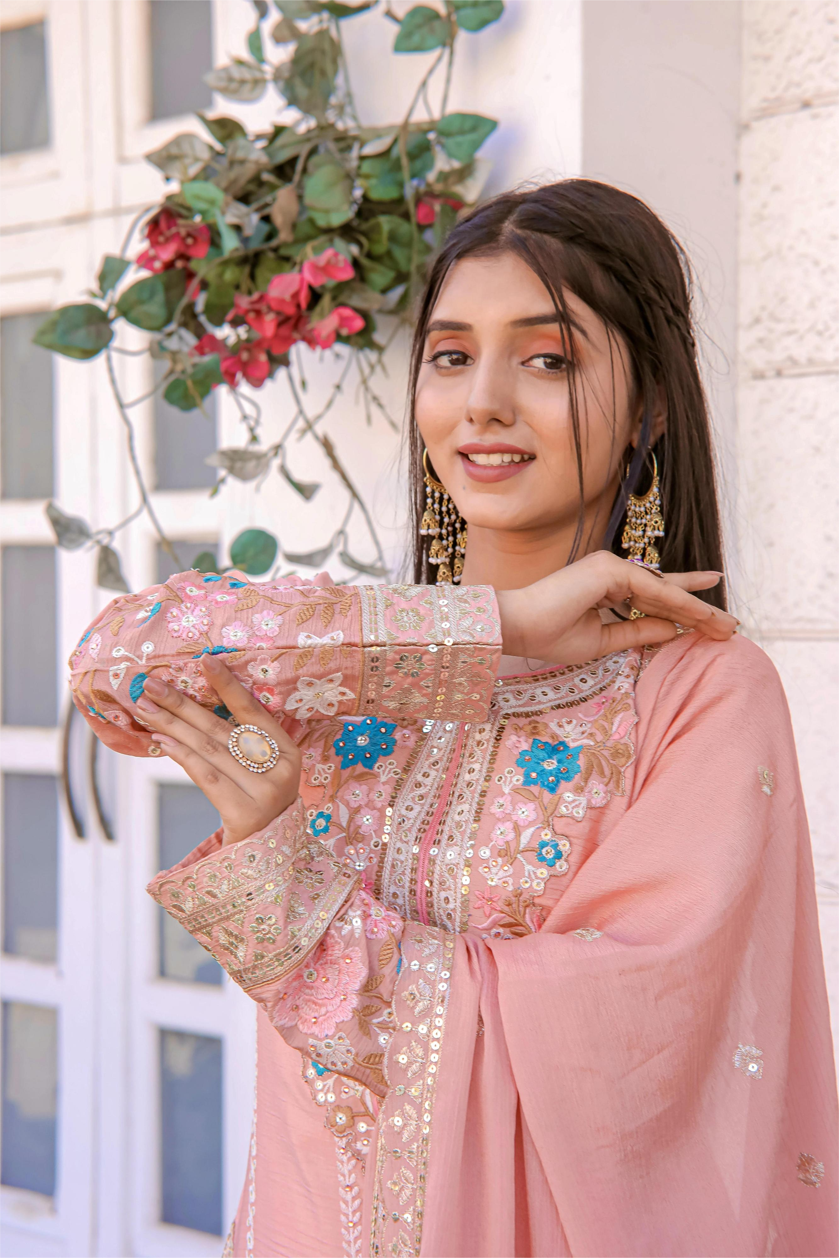 Woman wearing a pink embroidered outfit with floral decorations in the background