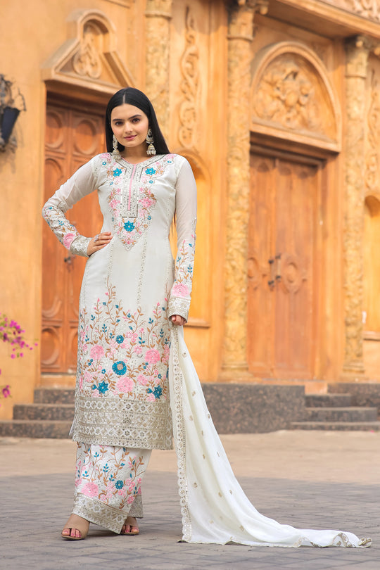 Woman in a traditional outfit with floral patterns standing in front of an ornate wooden door.