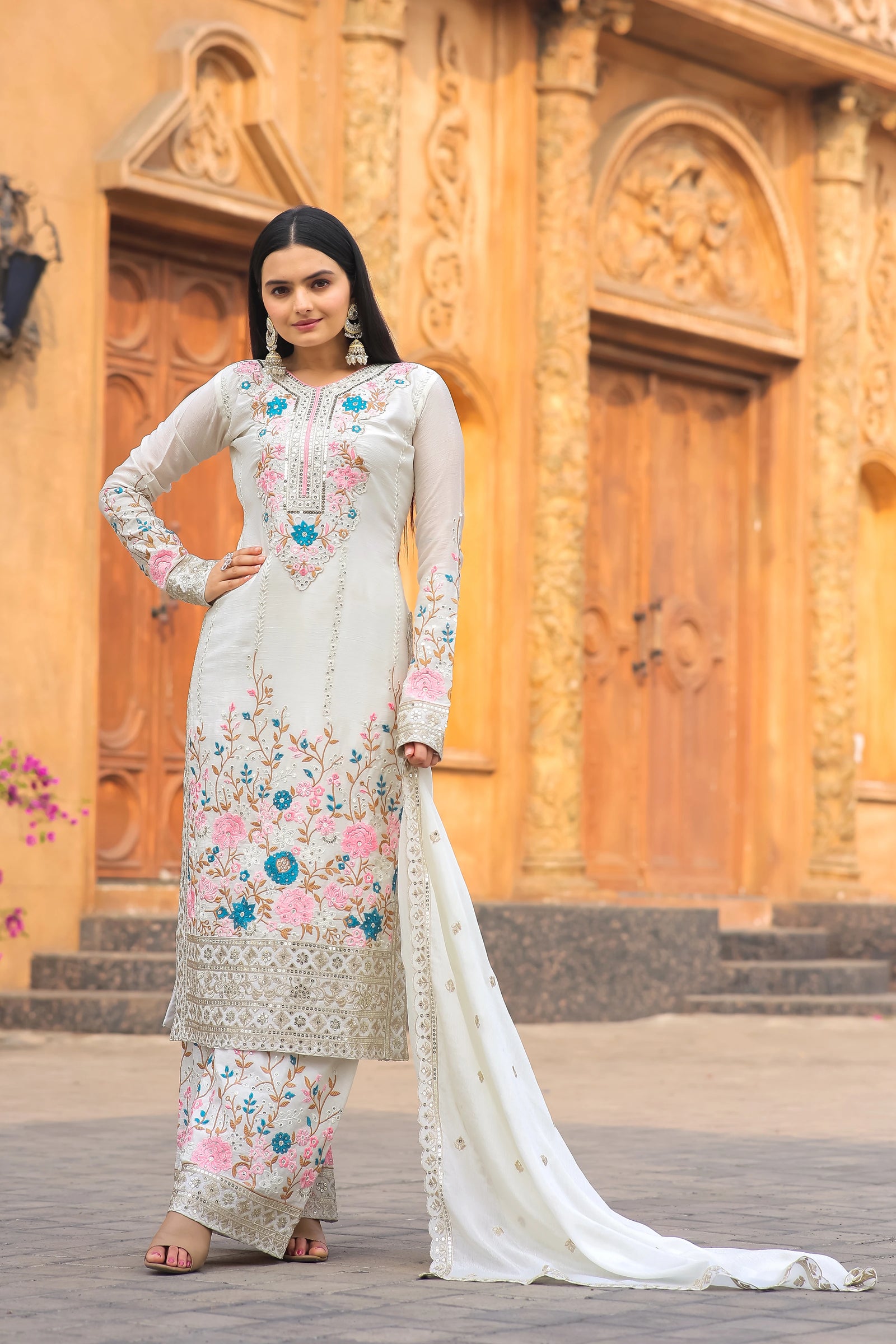 Woman in a traditional outfit with floral patterns standing in front of an ornate wooden door.