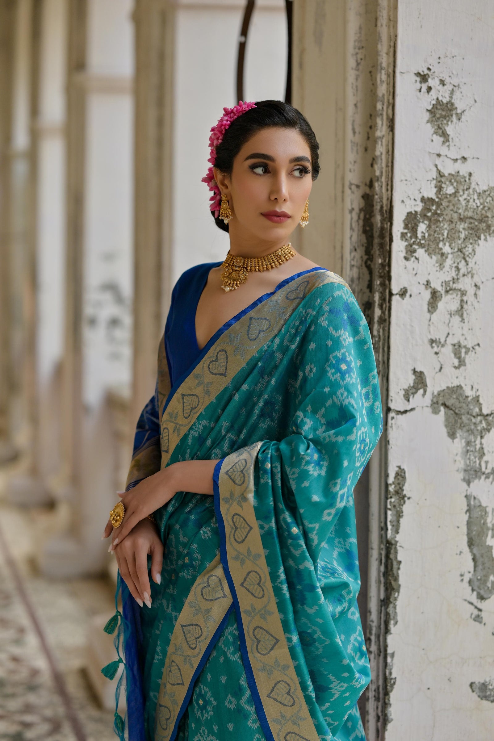 Woman wearing teal Pochampali Ikkat saree with zari weaving, styled in a regal setting with timeless grace