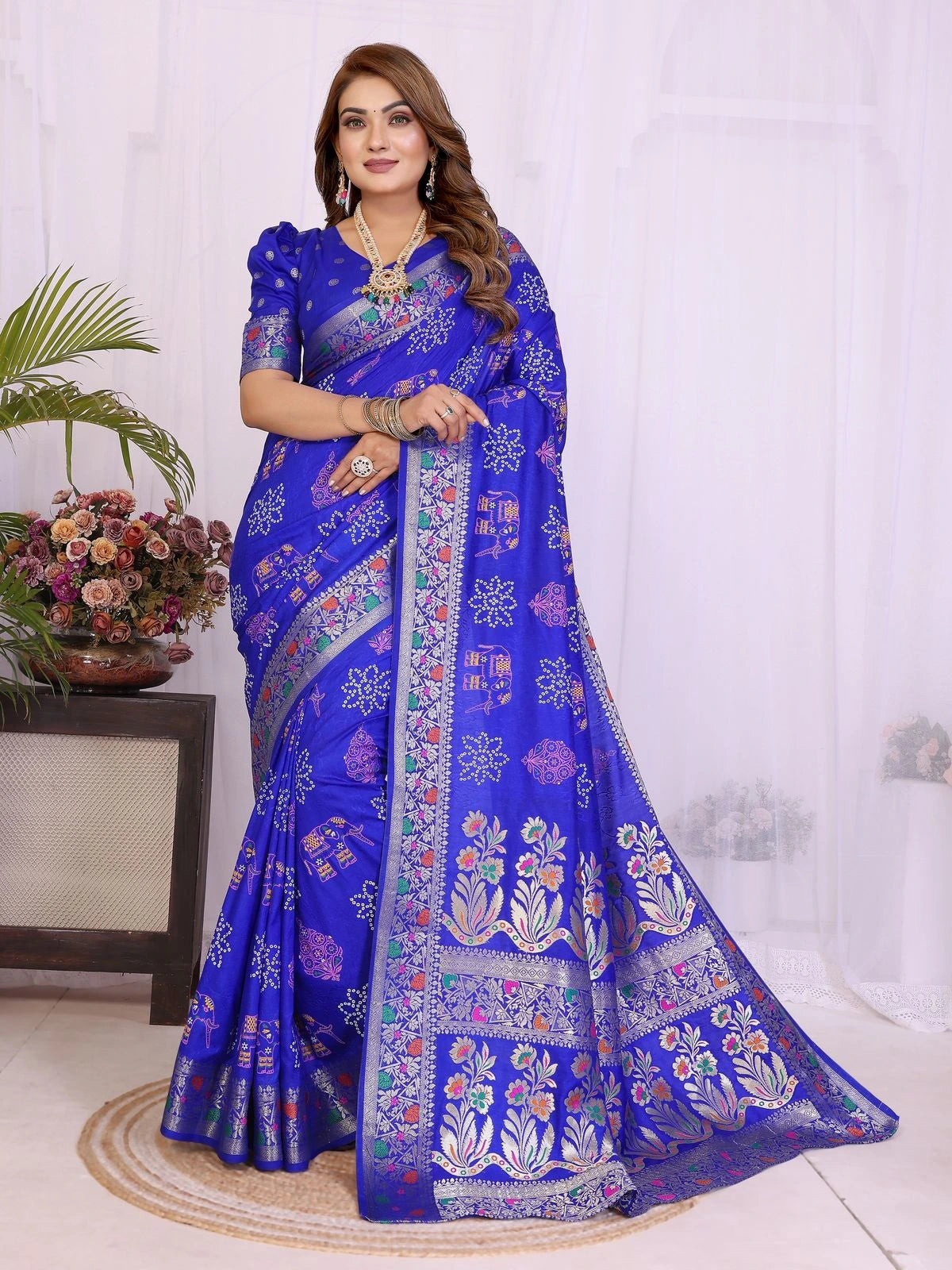 Woman wearing a blue saree with floral patterns in a room setting.