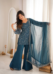 Woman holding a blue traditional outfit with a matching dupatta in a well-lit room.