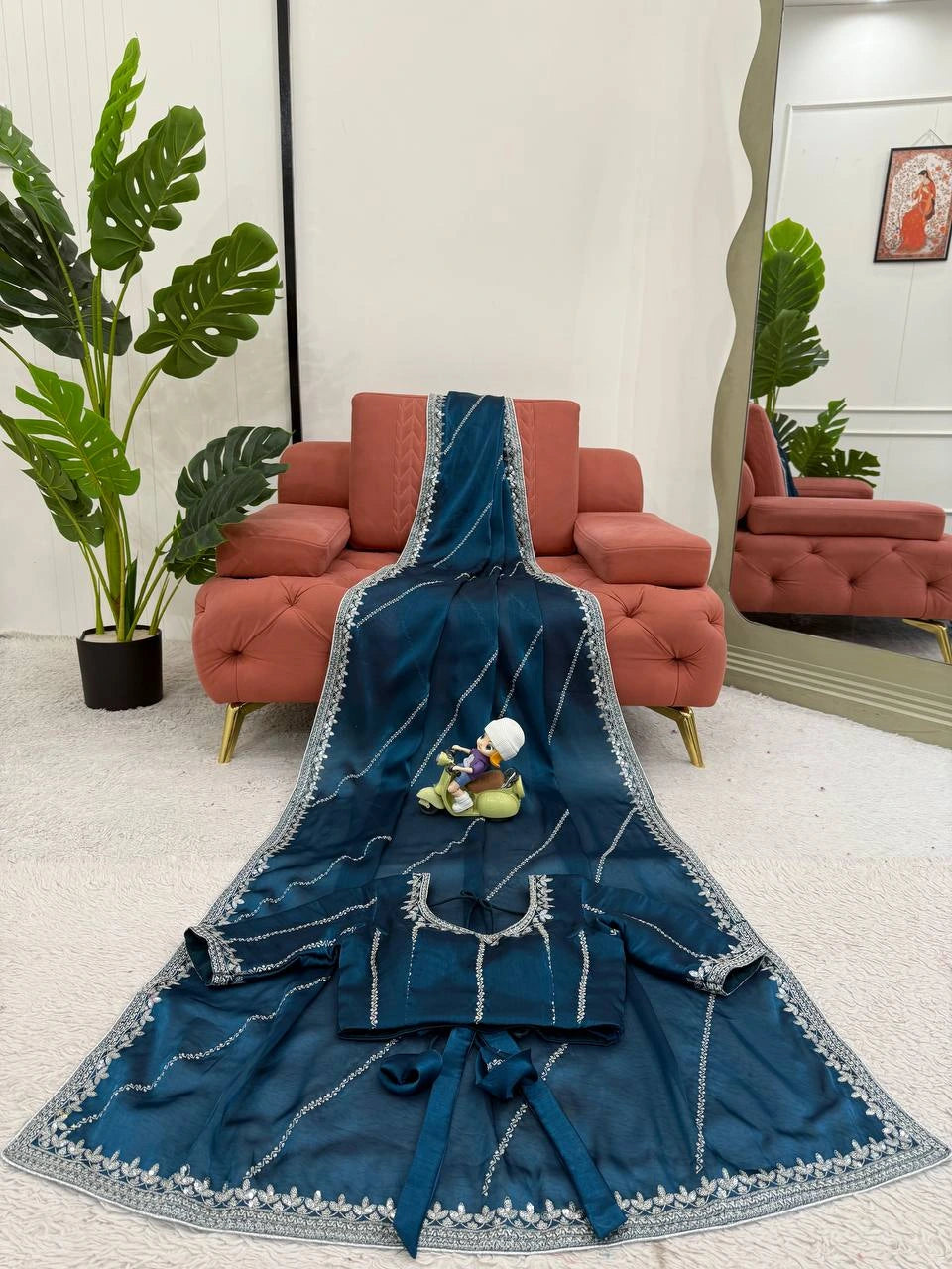 Blue embroidered garment on a white surface with a red sofa and green plants in the background
