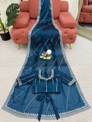 Blue embroidered garment on a white surface with a red couch in the background