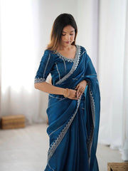 Woman wearing a blue saree with silver embroidery in a bright room.