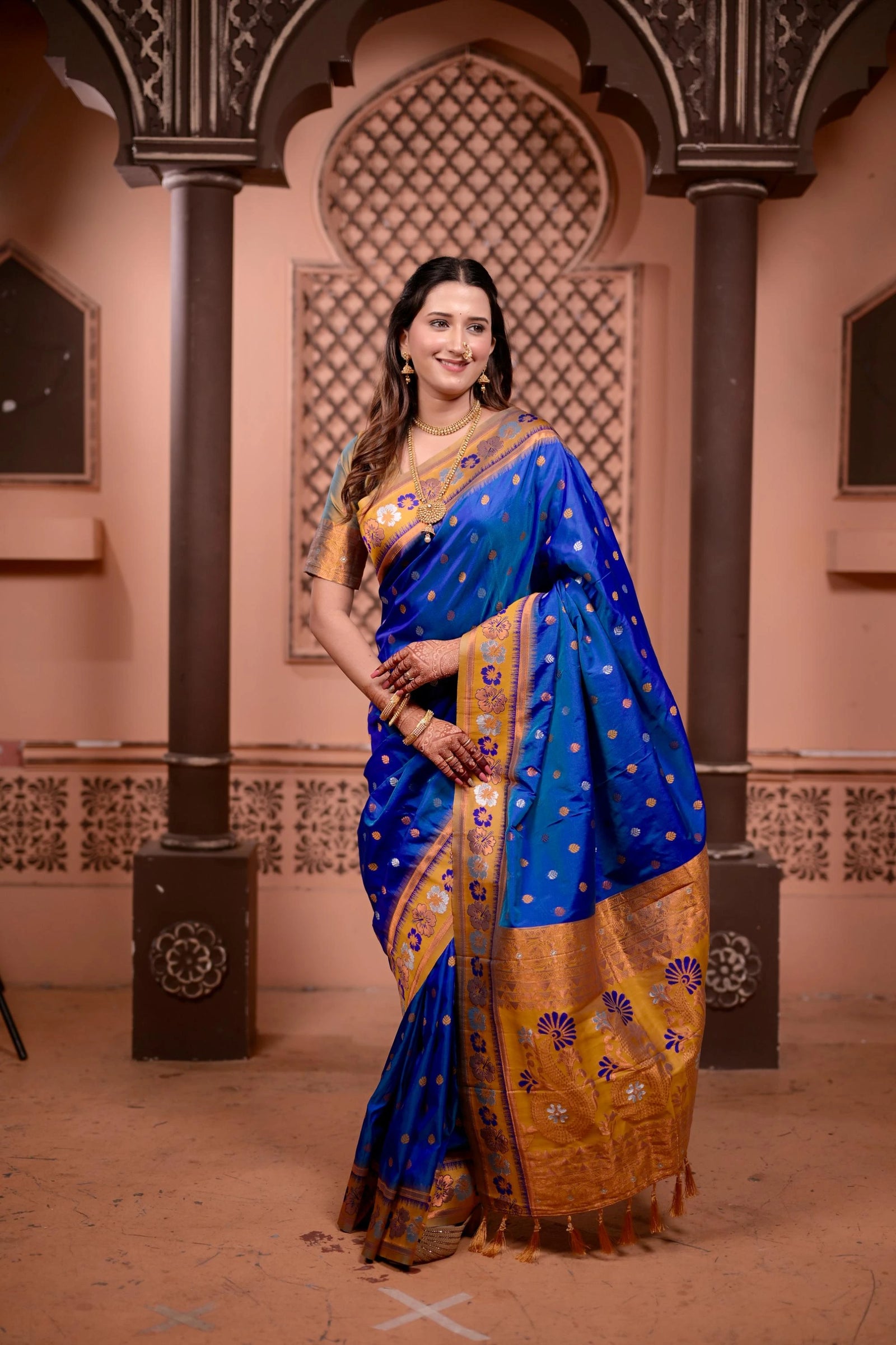 Woman in a blue and gold saree standing in an ornate indoor setting