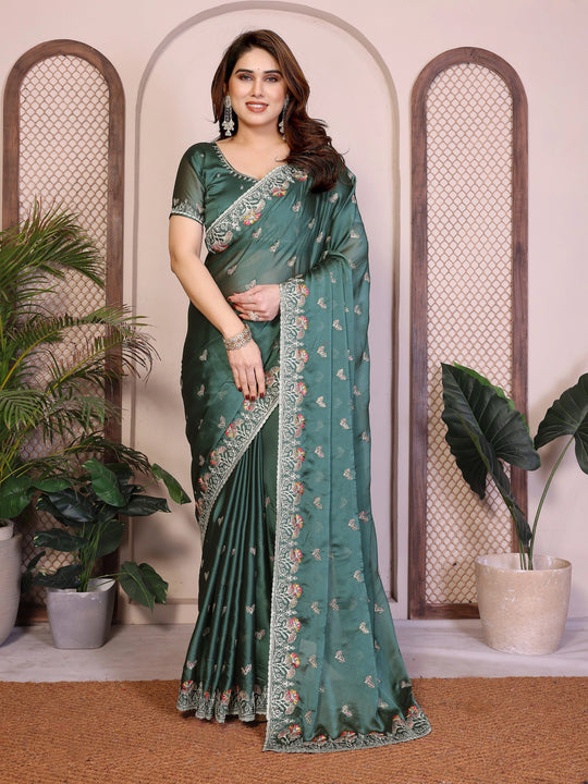 Woman wearing a green saree with floral patterns in an indoor setting with plants.