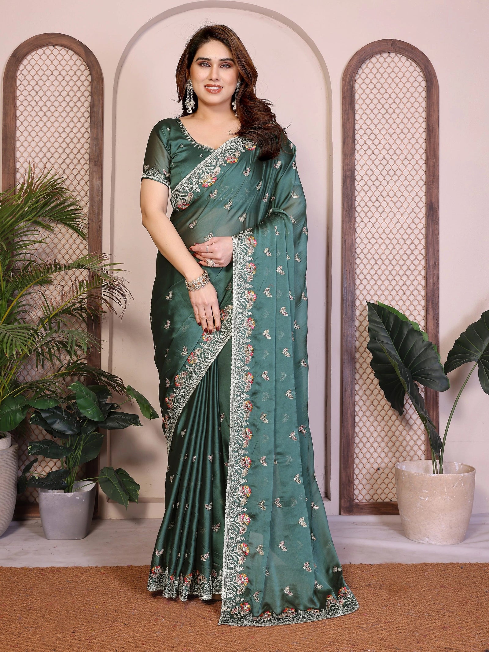 Woman wearing a green saree with floral patterns in an indoor setting with plants.