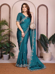 Woman wearing a teal saree with silver embroidery in an indoor setting with plants.