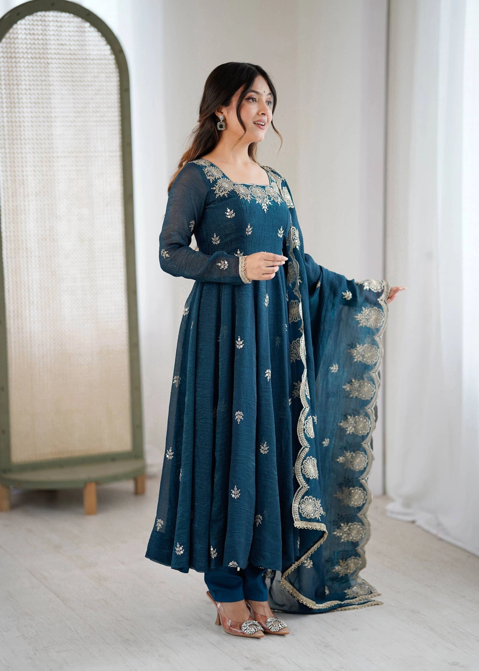 Woman in a teal traditional outfit with white patterns indoors.
