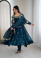 Woman in a blue traditional outfit with white patterns standing indoors.