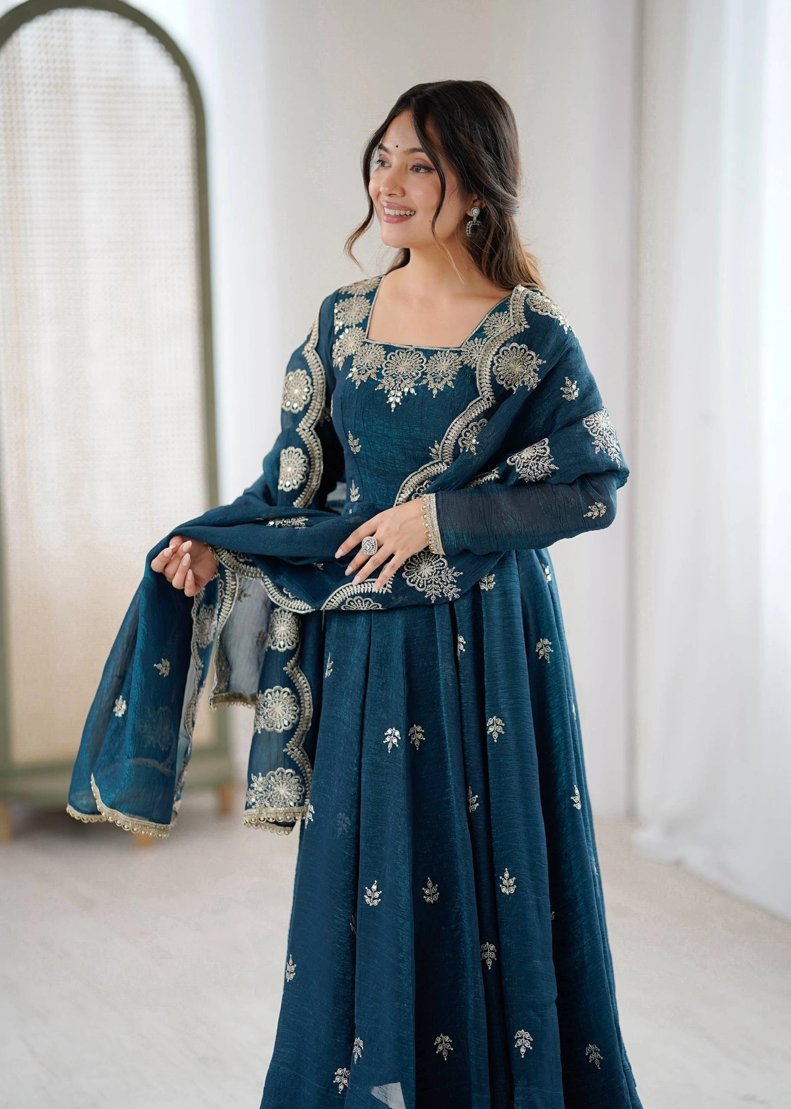 Woman wearing a teal embroidered dress in a minimal indoor setting
