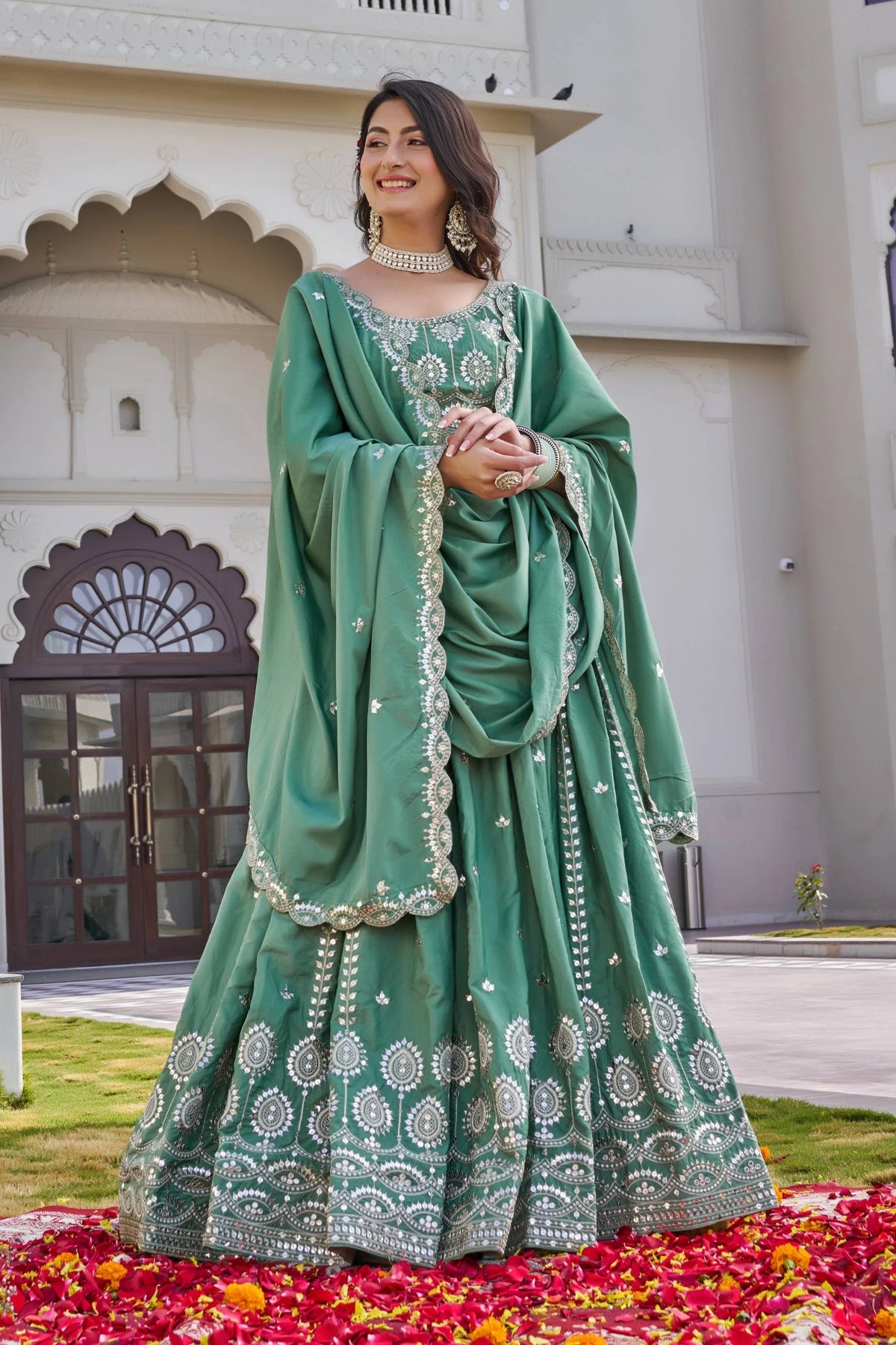 Woman in a green traditional outfit standing on a carpet of flowers with a building in the background