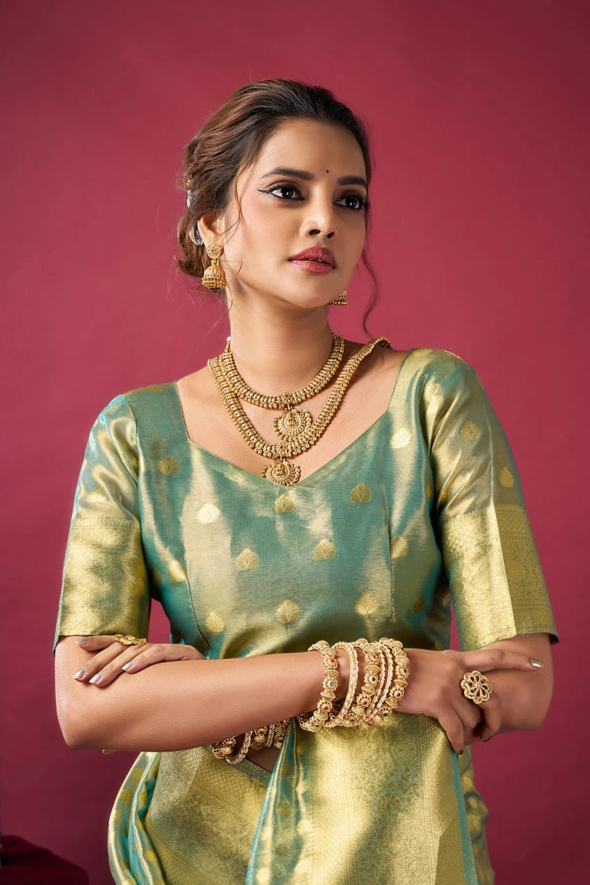 Woman in traditional green and gold outfit with jewelry against a pink background