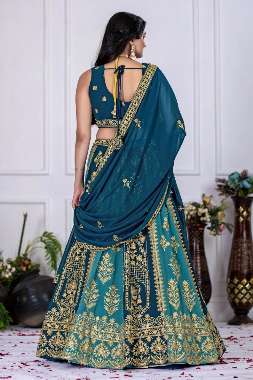 Woman in a teal and gold embroidered saree with a white wall background