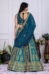 Woman in a teal and gold embroidered saree with a white wall background