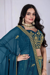 Woman wearing a teal saree with gold embroidery against a white background