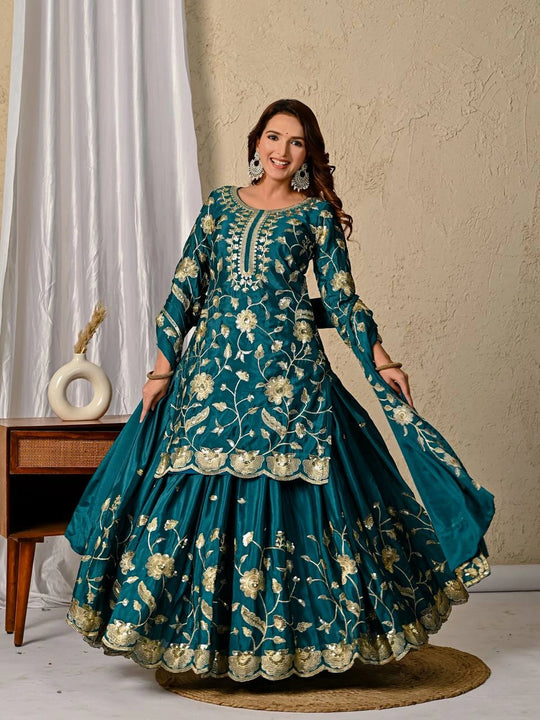 Woman wearing a teal embroidered traditional outfit with a beige background