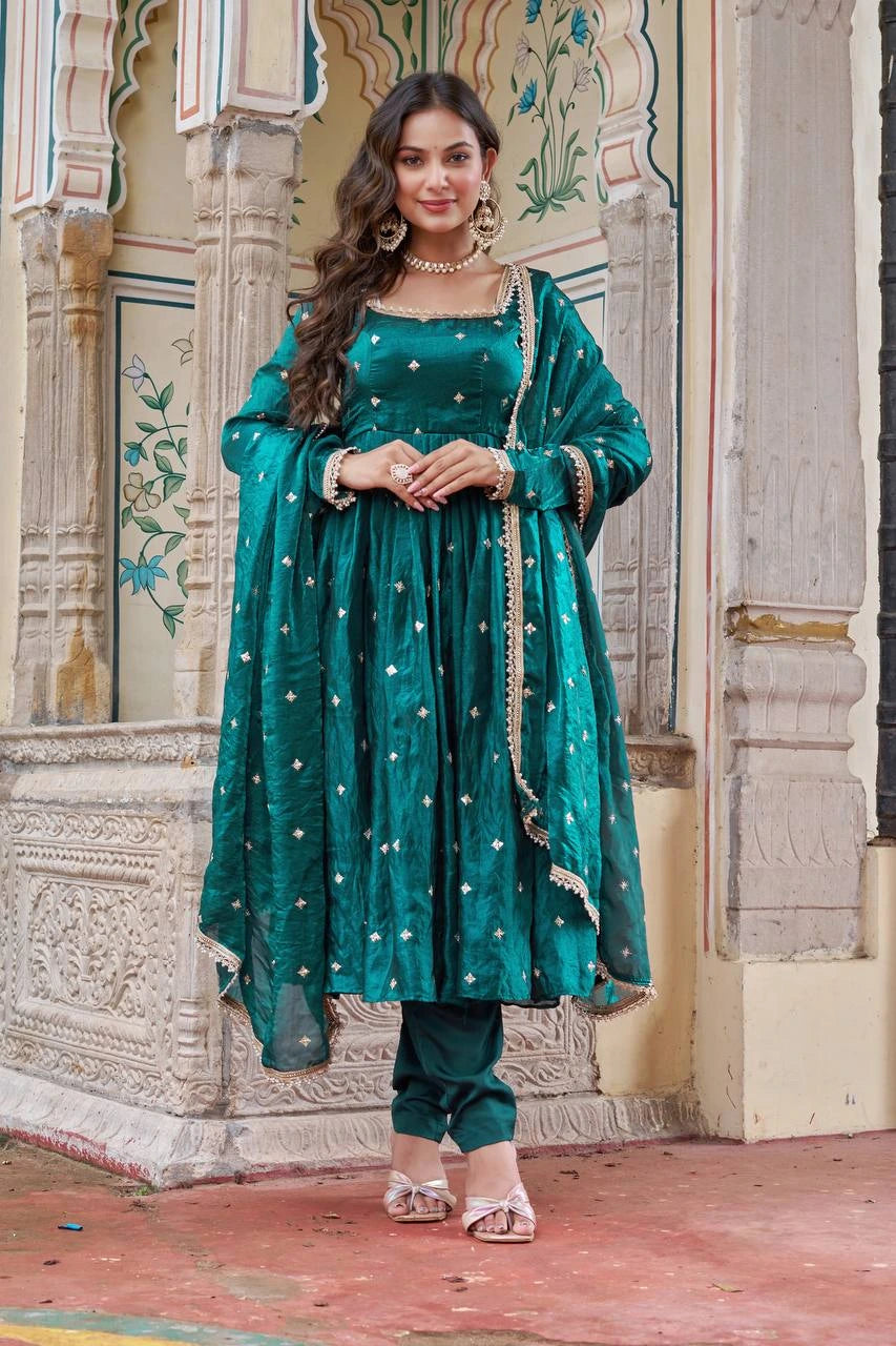 Woman in a teal traditional outfit standing in front of decorative architecture.