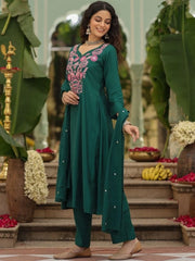 Woman in a green embroidered outfit standing outdoors with decorative elements.