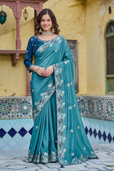 Woman in a teal saree with silver embroidery standing in front of a decorative building.