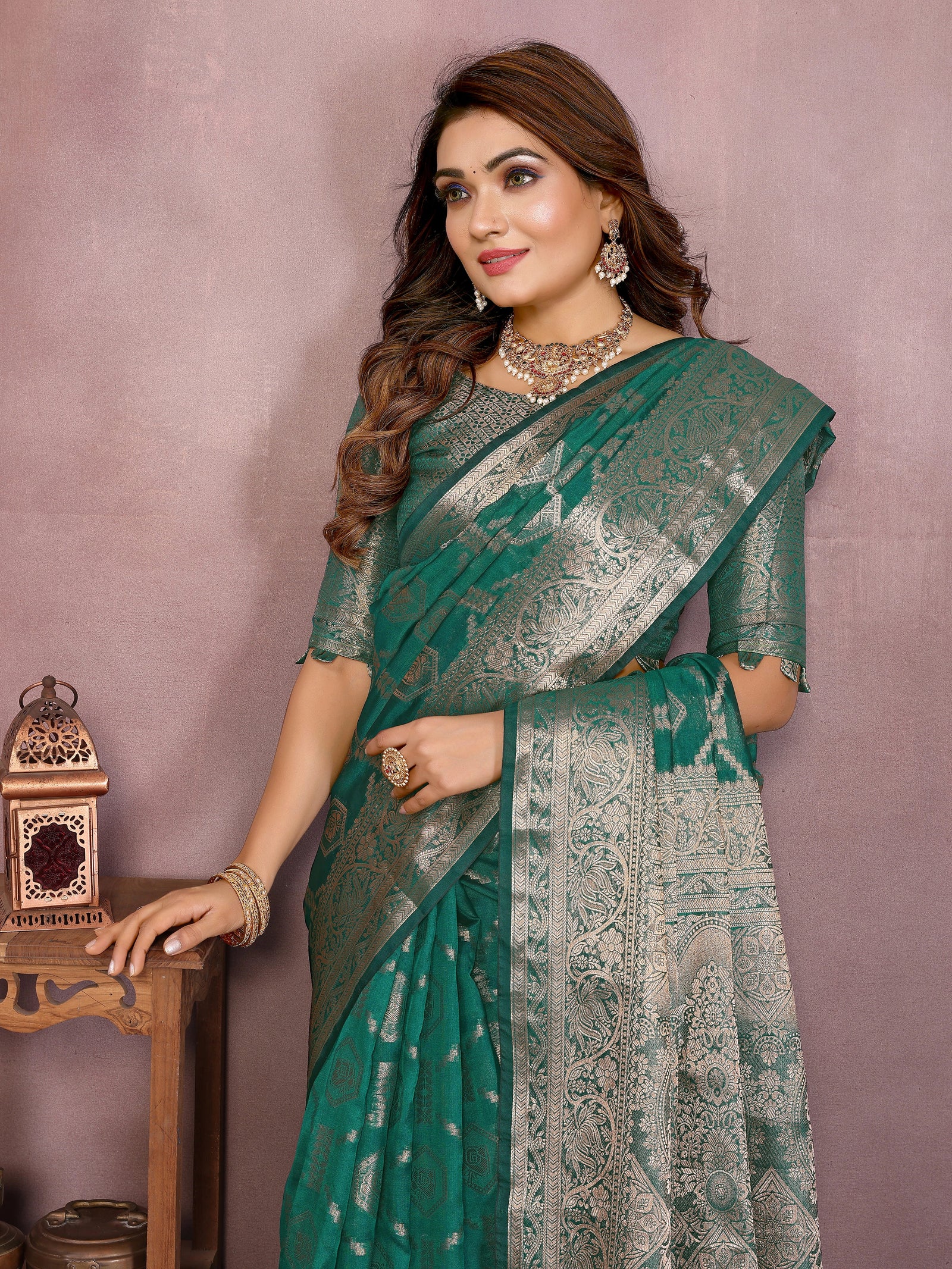 Woman wearing a green saree with a patterned blouse against a pink background