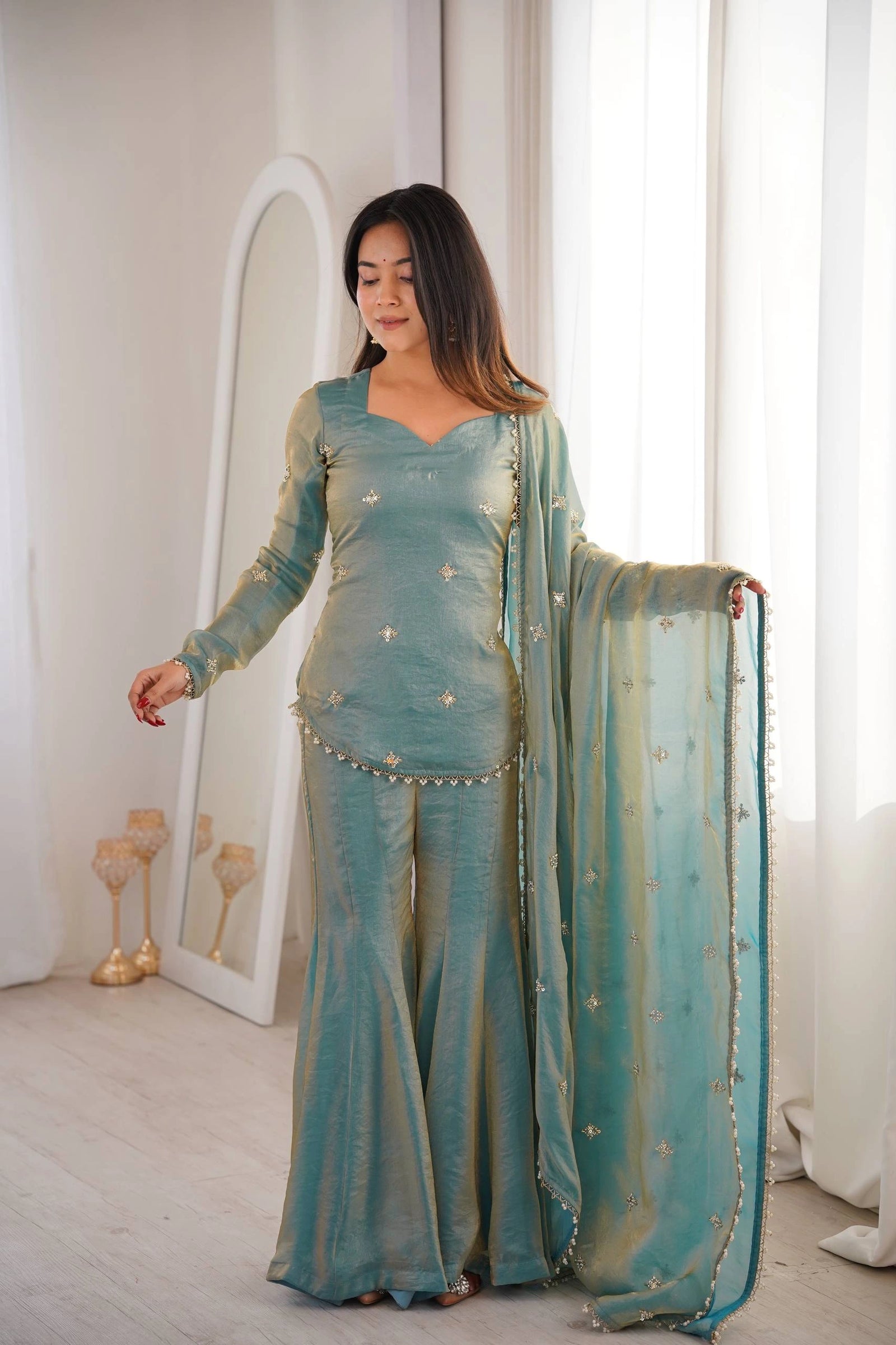 Woman wearing a teal traditional outfit with a matching dupatta in a bright room.