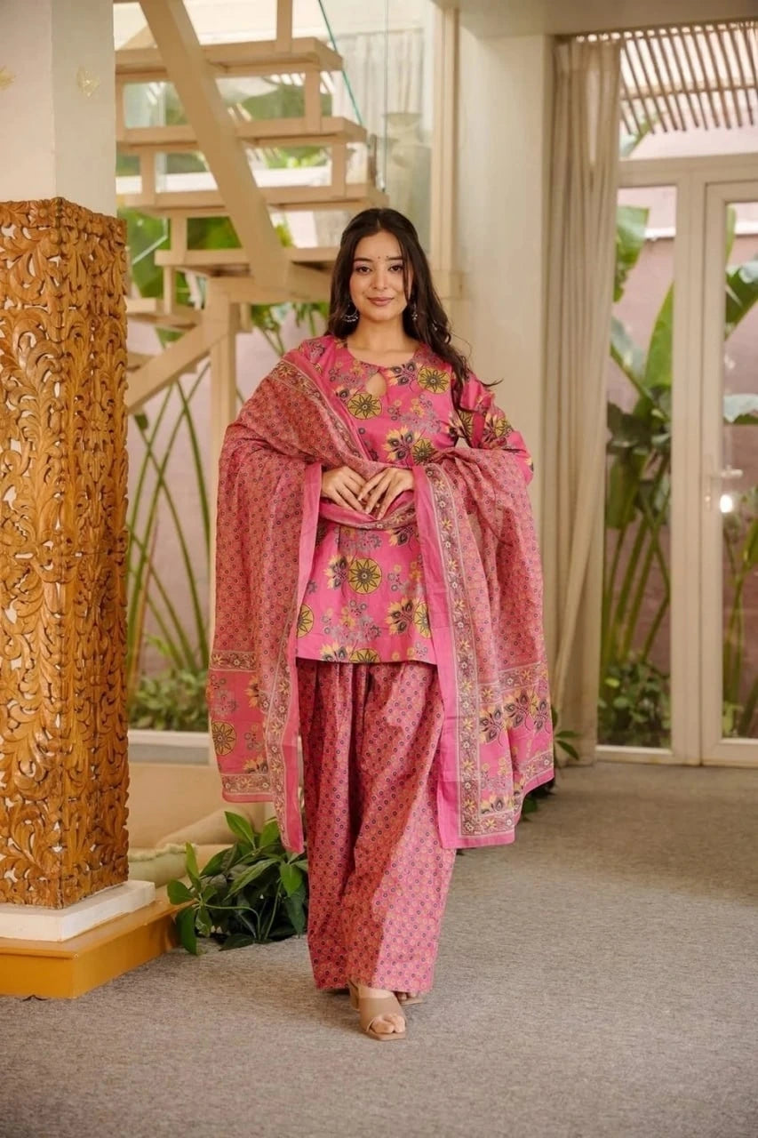 Woman in a pink traditional outfit standing indoors with decorative elements in the background