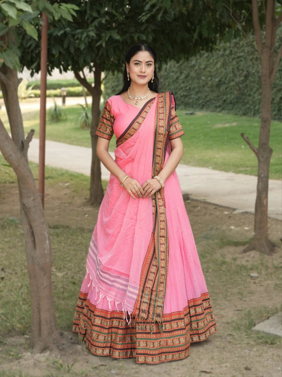 Woman wearing a pink saree with a traditional design in an outdoor setting