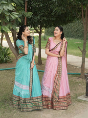 Two women in traditional sarees standing outdoors with trees and grass in the background.
