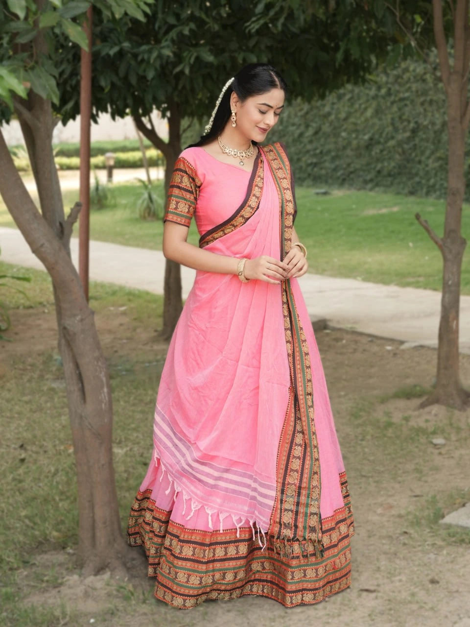Woman wearing a pink saree with a traditional design outdoors.