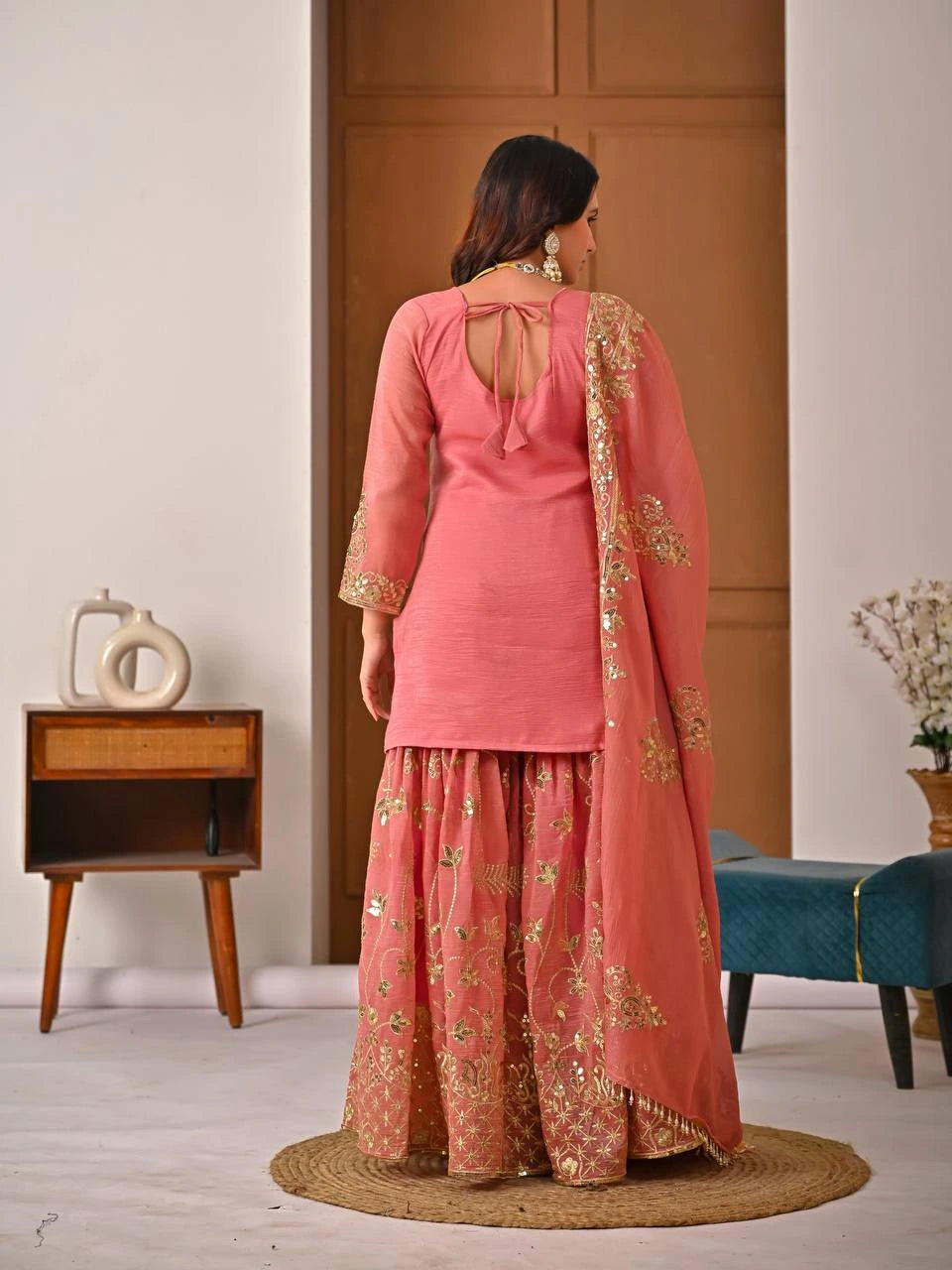 Woman in a pink traditional outfit with gold embroidery standing in a room.