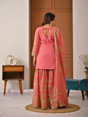 Woman in a pink traditional outfit with gold embroidery standing in a room.