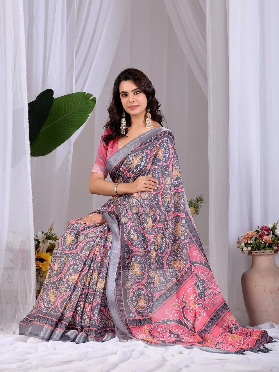 Woman wearing a pink and gray saree with a white curtain and plant in the background