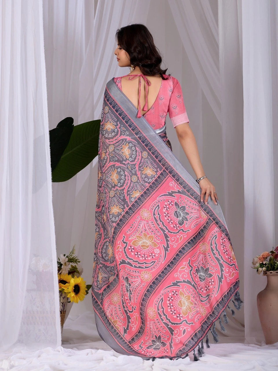 Woman wearing a pink and gray saree with a white curtain background